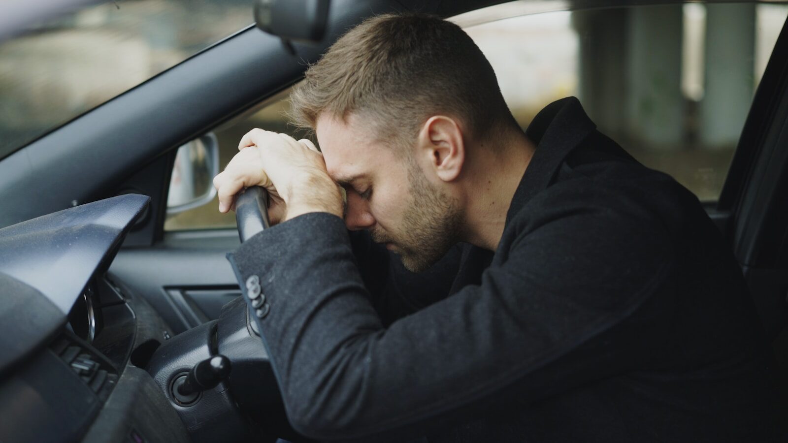 Man resting head on steering wheel in car